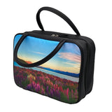 A rectangular vanity/cosmetic case with 2 black handles. The front and back of the cosmetic case display a beautiful scene of pink and purple lupins, with New Zealand’s spectacular mountain ranges in the background, under a blue sky with wispy clouds. The sides are black, with a black zip around 3 sides. 