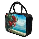 A rectangular vanity/cosmetic case with 2 black handles. The front and back of the cosmetic case display a Kiwi summer scene of blooming Pohutukawa tree with red flowers surrounded by green leaves, and a hot Summer’s day beach in the background with clear waters, white sand and a blue sky with wispy clouds. The sides are black, with a black zip around 3 sides. 