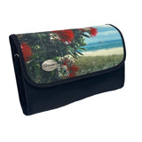 A rectangular cosmetic bag with which secures with a Velcro strip across the top. The front of the bag displays a Kiwi summer scene of blooming Pohutukawa tree with red flowers surrounded by green leaves, and a hot Summer’s day beach in the background with clear waters, white sand and a blue sky with wispy clouds. The front left corner hosts a silver badge with the AA Traveller logo. The back and sides are black, with a black Velcro strip and unfolds into 4 compartments. 