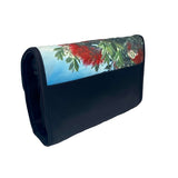 A rectangular cosmetic bag with which secures with a Velcro strip across the top. The front of the bag displays a Kiwi summer scene of blooming Pohutukawa tree with red flowers surrounded by green leaves, and a hot Summer’s day beach in the background with clear waters, white sand and a blue sky with wispy clouds. The back and sides are black, with a black Velcro strip and unfolds into 4 compartments. 